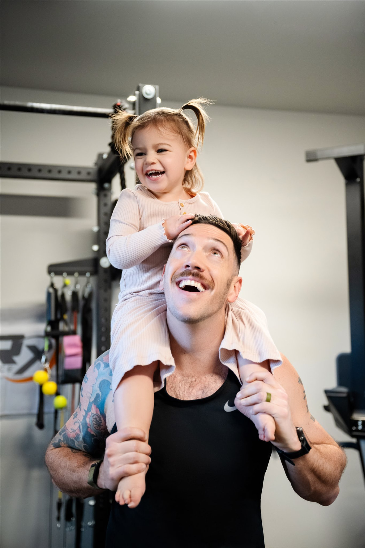 Sean in his home gym with his daughter on his shoulders, both laughing